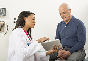 Healthcare provider with digital tablet talking to man.