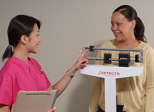 Health care provider weighing woman on scale.