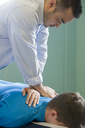Un quiropráctico trabaja sobre el cuello y la zona del hombro de un hombre recostado en una camilla.