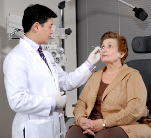 Mujer sentada en una silla de examen. El proveedor de atención médica está examinándole el ojo.