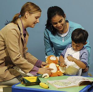 Un proveedor de atención médica y una mujer que observan cómo un niño juega con juguetes médicos.