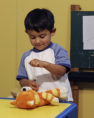 Niño que juega con una jeringa de juguete y un osito de peluche.
