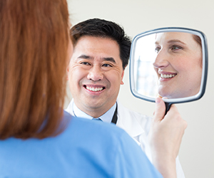 Mujer mirando su reflejo en un espejo de mano y proveedor de atención médica observando.