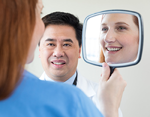 Mujer mirando su reflejo en un espejo de mano y proveedor de atención médica observando.