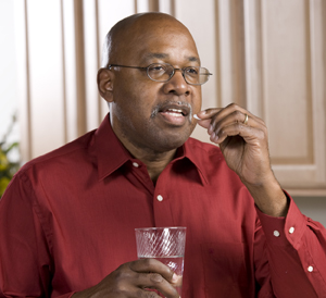 Hombre que se coloca una pastilla en la boca mientras sostiene un vaso de agua.