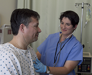 Proveedora de atención médica usando un estetoscopio sobre el pecho de un hombre en la cama de un hospital.