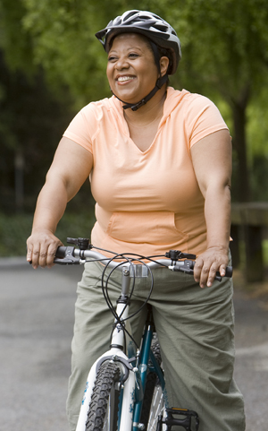Overweight woman riding a bicycle on a country road.