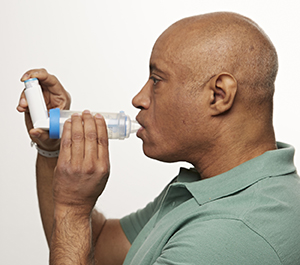 Man using metered-dose inhaler with spacer.