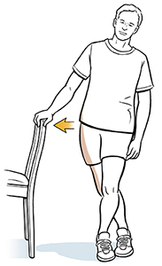 Man leaning on a chair while elongating the hip by stretching the iliotibial band.