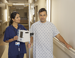Patient walking in hospital hall with an IV pole and healthcare provider.