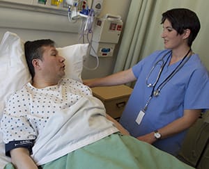 Man in hospital bed talking to health care provider.