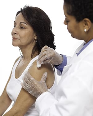 Health care provider preparing to give woman shot in arm.