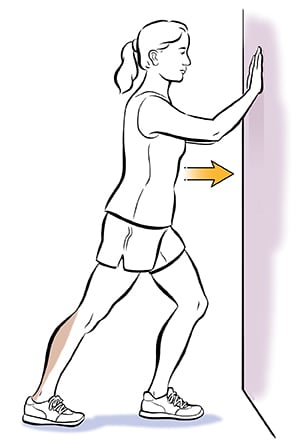 Person leaning hands on wall doing calf stretch.