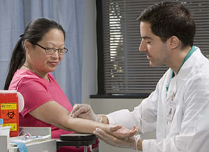 Health care provider preparing to take blood from woman’s arm.