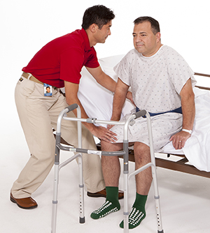 Healthcare provider helping man stand up from hospital bed. Walker next to bed.