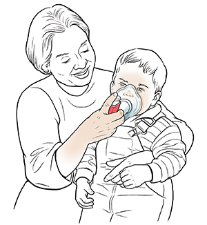 Woman holding toddler boy on lap helping him breathe through mask with metered-dose inhaler.