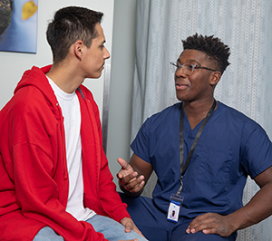 Proveedor de atención médica hablando con un adolescente en la sala de examinación.