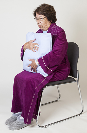 Mujer sentada y sosteniendo un almohada contra su pecho.