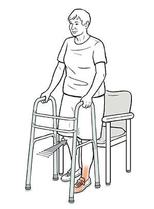 Mujer con un andador retrocediendo hacia una silla, con una mano en el andador y la otra en el apoyabrazos de la silla. La silla está en contacto con la parte posterior de sus piernas.