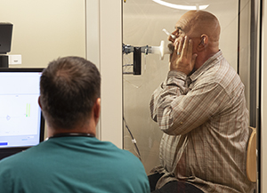 Un técnico le realiza pruebas de función pulmonar a un hombre en una cabina de prueba.