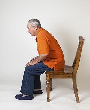 Hombre sentado en el borde delantero de una silla, preparándose para ponerse de pie.