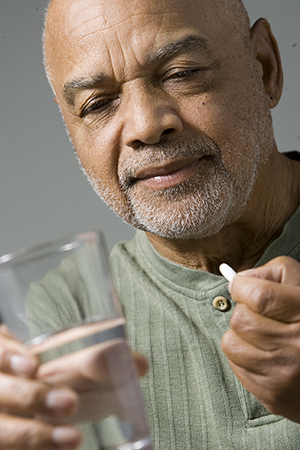 Hombre sosteniendo una píldora y un vaso con agua.