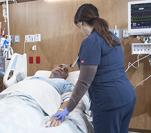 Proveedor de atención médica atendiendo a un hombre en una cama de la unidad de cuidados intensivos.