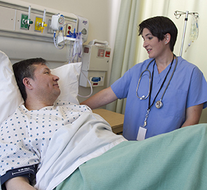 Hombre en una camilla de hospital hablando con un proveedor de atención médica.