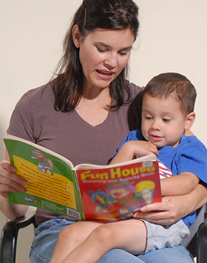 Mujer que sostiene a un niño pequeño sobre su regazo, mientras lee.