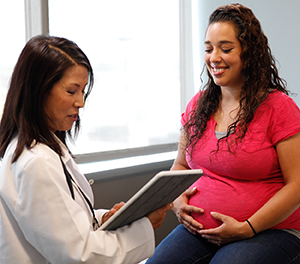 Mujer embarazada sentada en una mesa de exámenes, hablando con un médico.