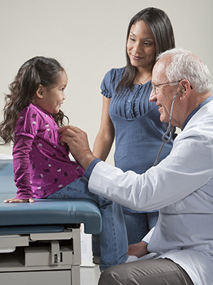 Proveedor de atención médica auscultando el pecho de una niña con un estetoscopio. Mujer parada cerca.